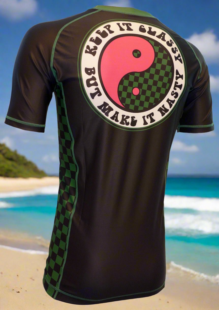 The Wave Hugger Classy and Nasty Rash Guard is a black short-sleeve top with green checkerboard panels, yin-yang graphic, and KEEP IT CLASSY BUT MAKE IT NASTY on the back—ideal for jiu jitsu or beach surfing.