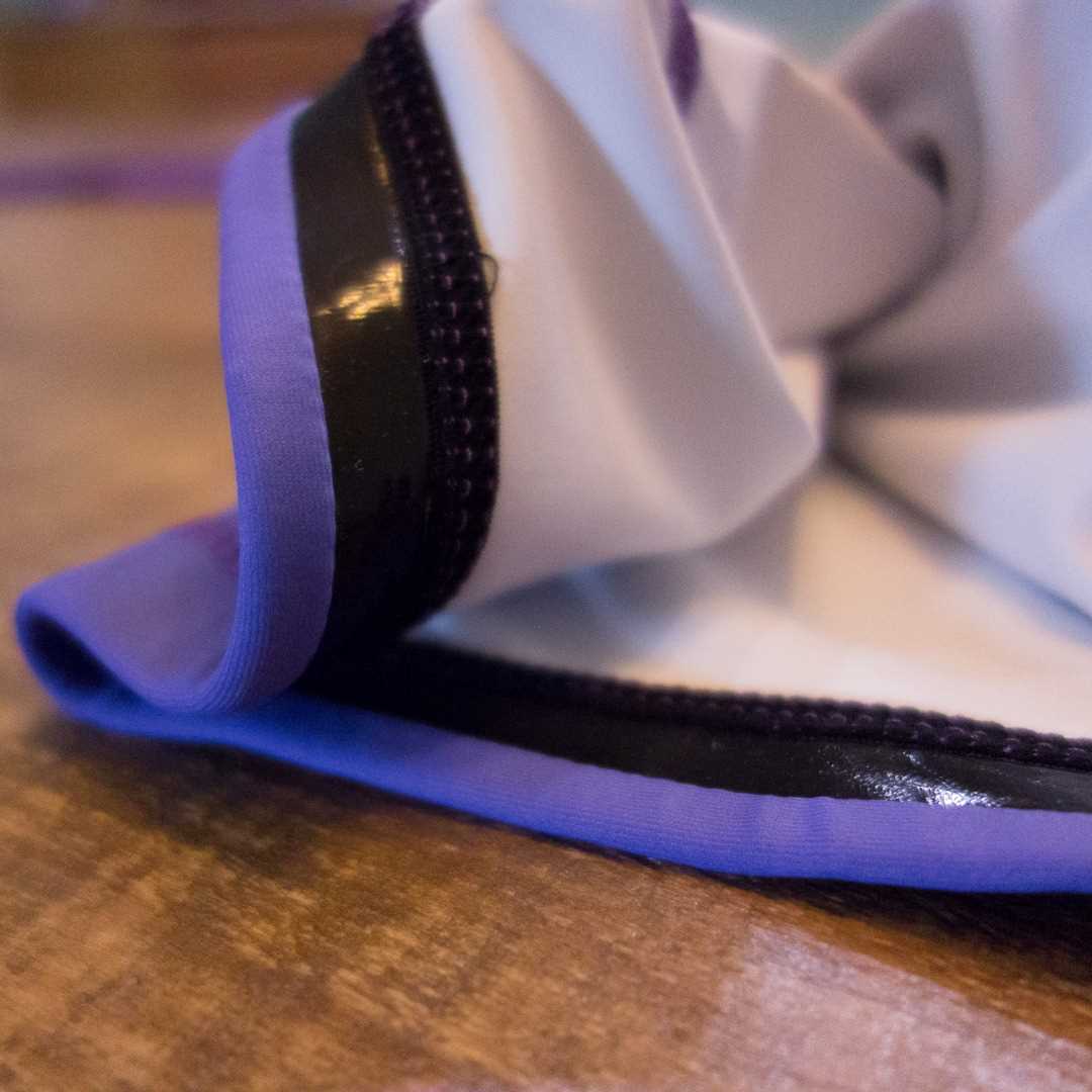 Close-up of the Face Crank 2 - Lisa Frank Parody BJJ Rash Guard by Retro Grappler, showing its rumpled fabric with a purple edge and black stripe, folded on wood—highlighting details typical of women’s BJJ rash guards.