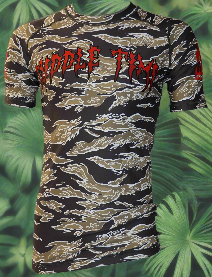 The Retro Grappler Cuddle Time Tiger Stripe Camo Rash Guard features a fitted short-sleeve design with brown, black, and white stripes, red CUDDLE TIME text on the chest, and a green tropical leaf background—ideal for BJJ rash guard collectors.
